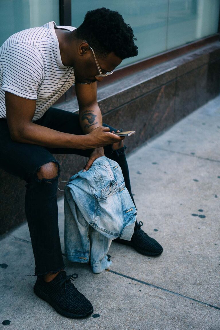 Man sitting on his phone holding a denim jacket