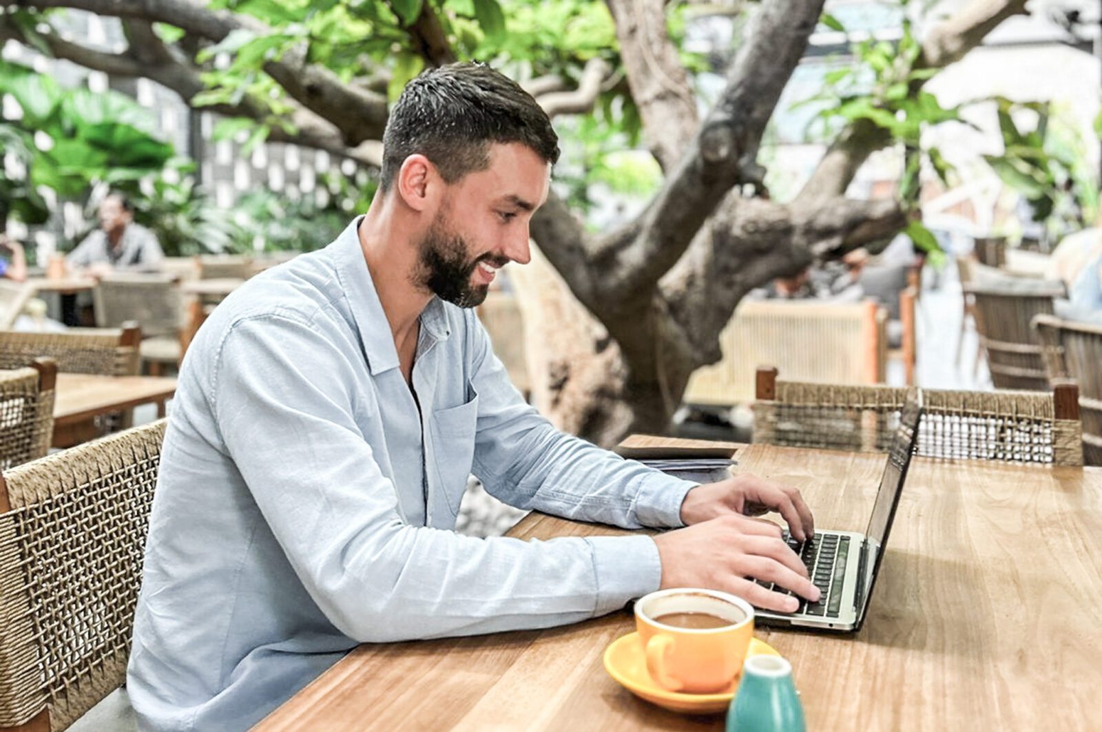 young man typing on notebook drinking coffee in cafe outdoor