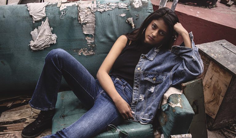 woman sitting on an old sofa wearing a denim jacket and jeans