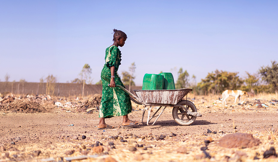 girl transporting water jugs in wheelbarrow